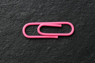 One pink paper clip on black table, top view