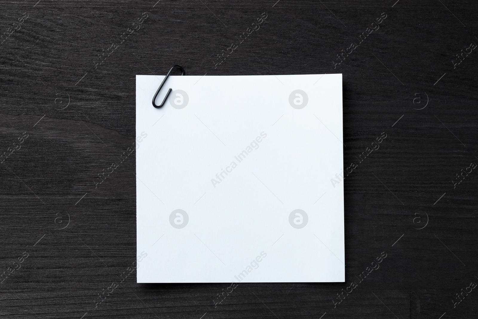 Photo of Paper note with clip on black wooden table, top view. Space for text