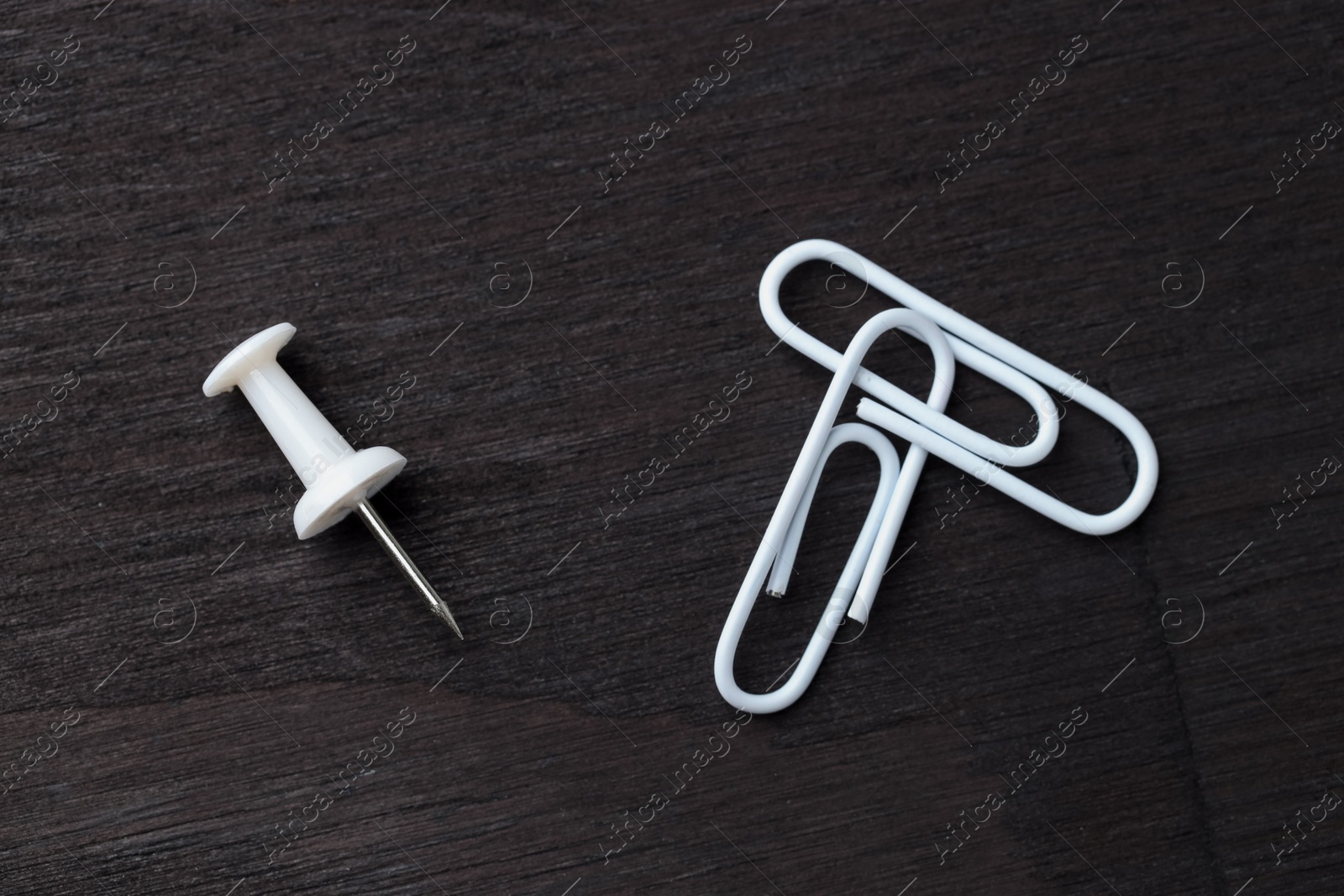 Photo of Two white paper clips and pin on black wooden table, flat lay