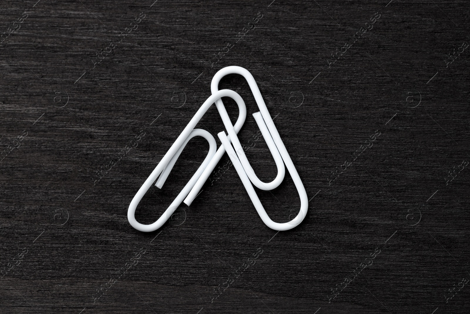 Photo of Two white paper clips on black wooden table, top view