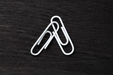 Photo of Two white paper clips on black wooden table, top view