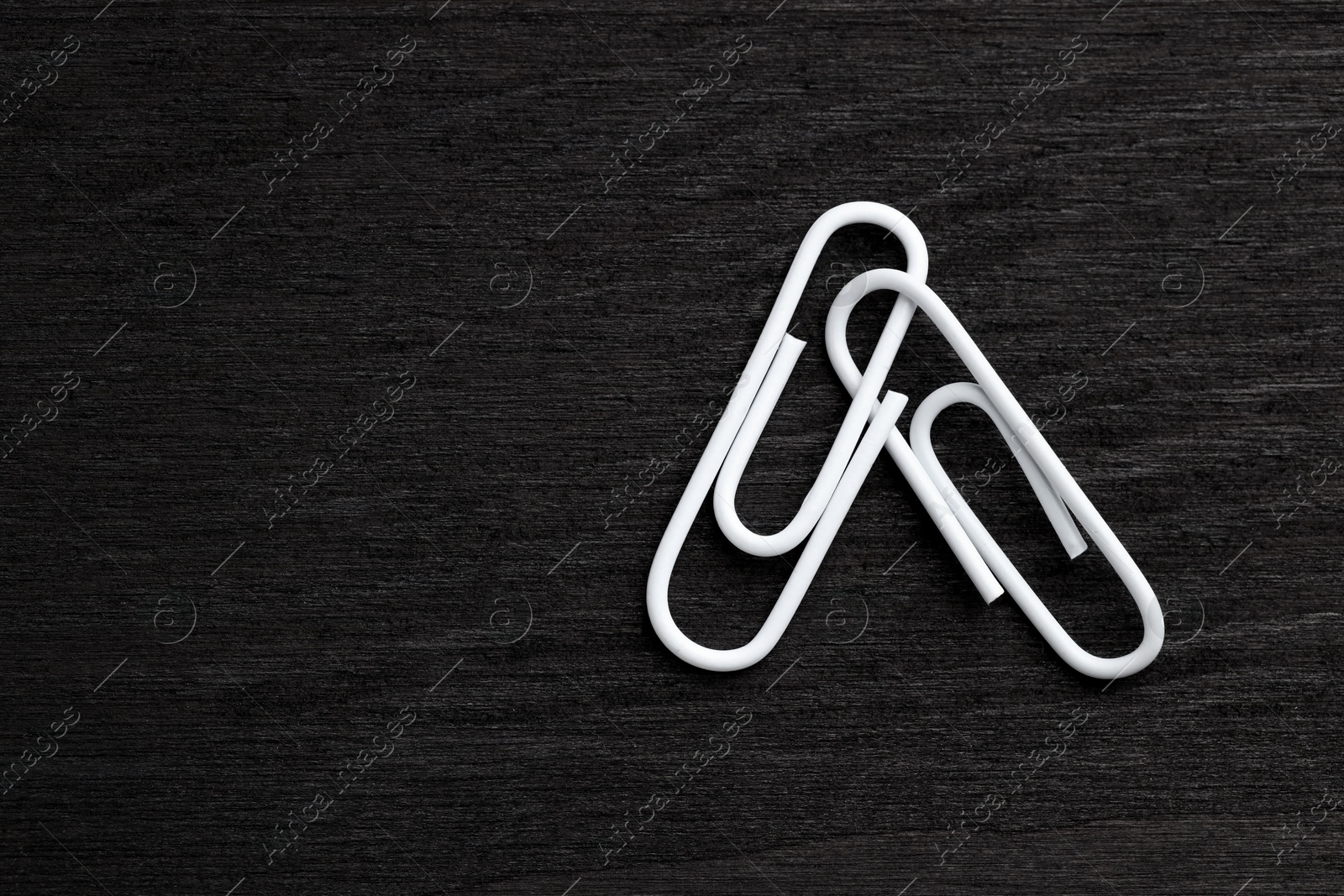 Photo of Two white paper clips on black wooden table, top view. Space for text