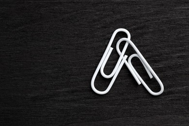 Two white paper clips on black wooden table, top view. Space for text