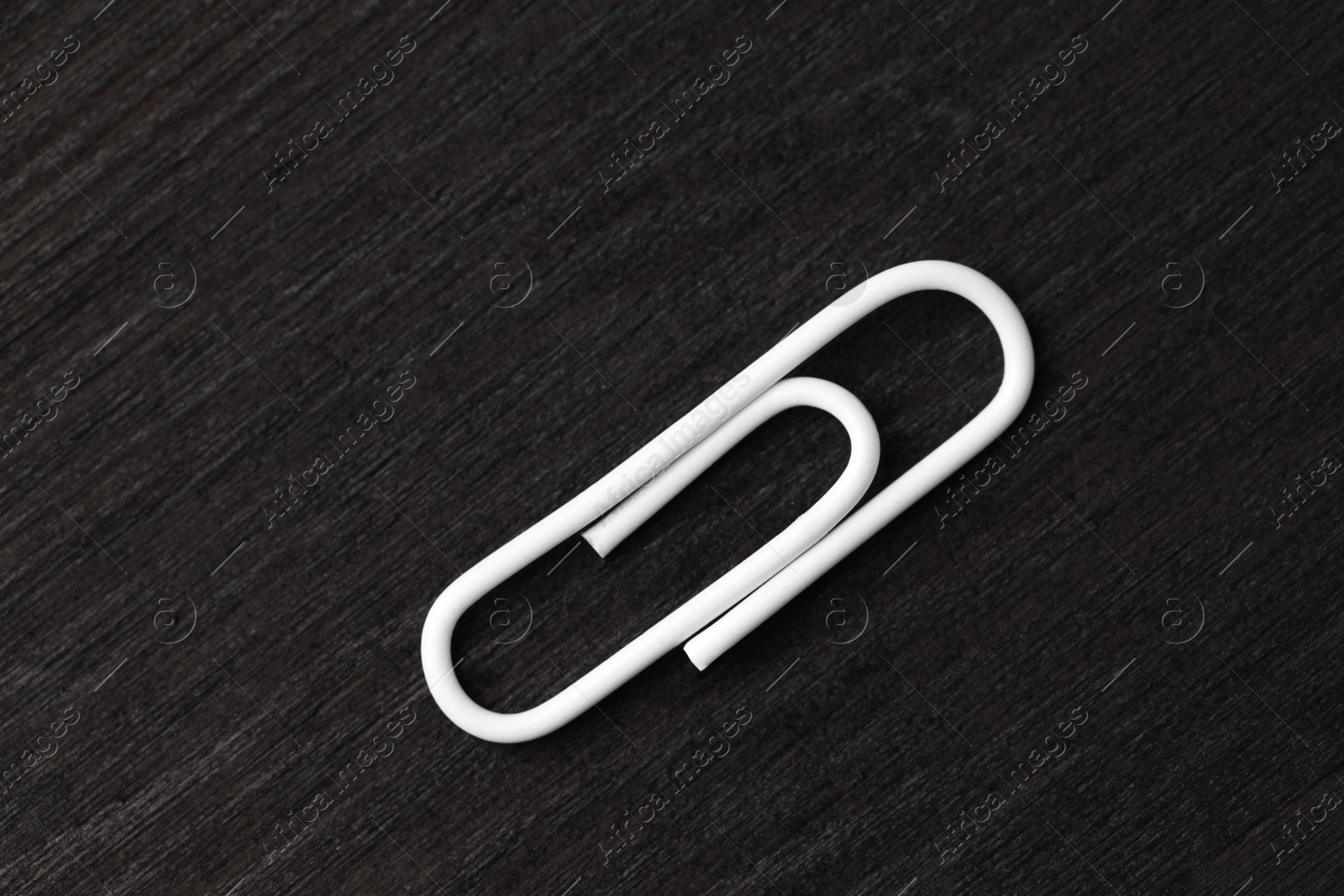 Photo of One white paper clip on black wooden table, top view