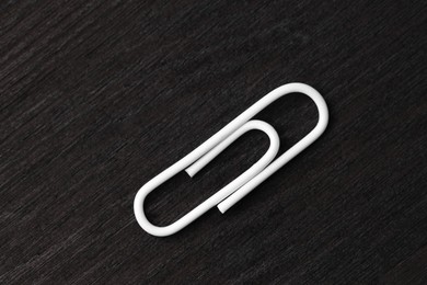 One white paper clip on black wooden table, top view