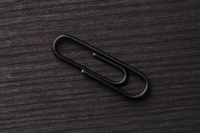 Photo of One black paper clip on wooden table, top view