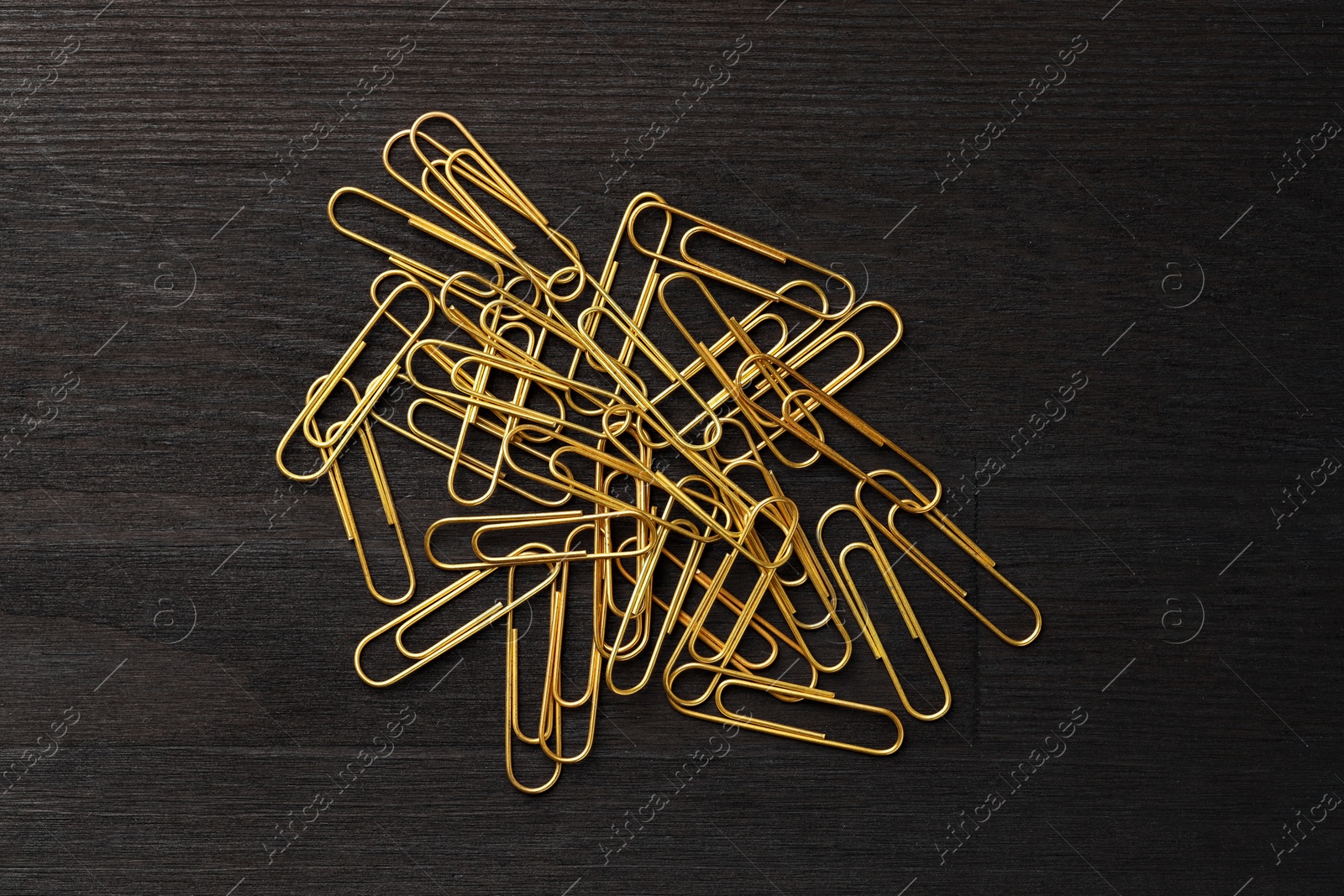 Photo of Many golden paper clips on black table, top view