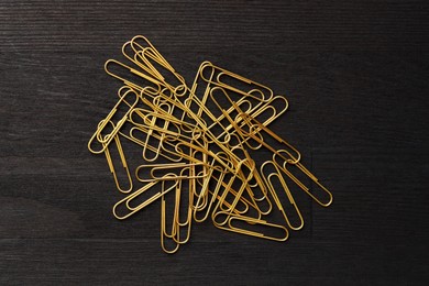 Many golden paper clips on black table, top view