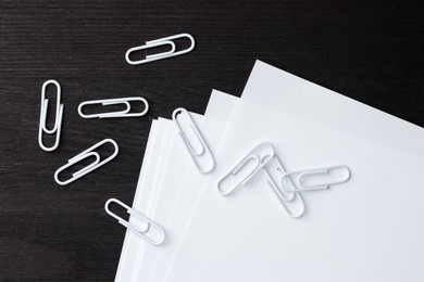 Many white clips and paper notes on black wooden table, flat lay