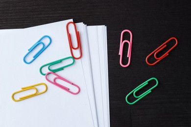 Many colorful clips and paper notes on black wooden table, flat lay