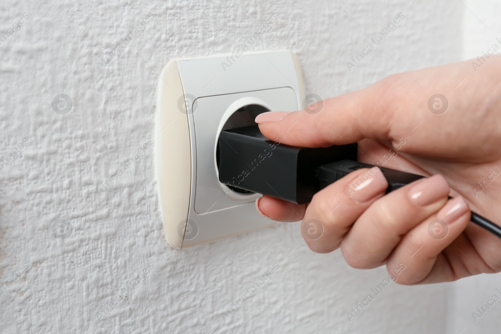 Photo of Woman plugging USB power adapter with charge cable into electrical socket indoors, closeup