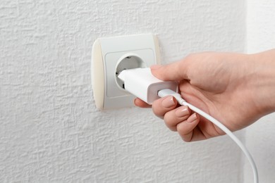 Photo of Woman plugging USB power adapter with charge cable into electrical socket indoors, closeup