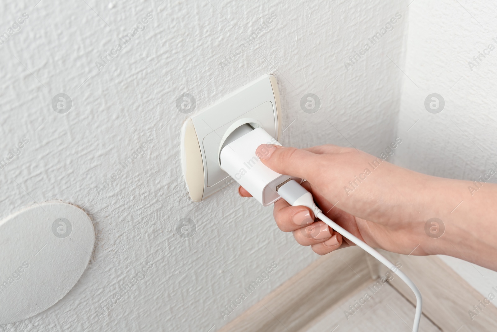 Photo of Woman plugging USB power adapter with charge cable into electrical socket indoors, closeup