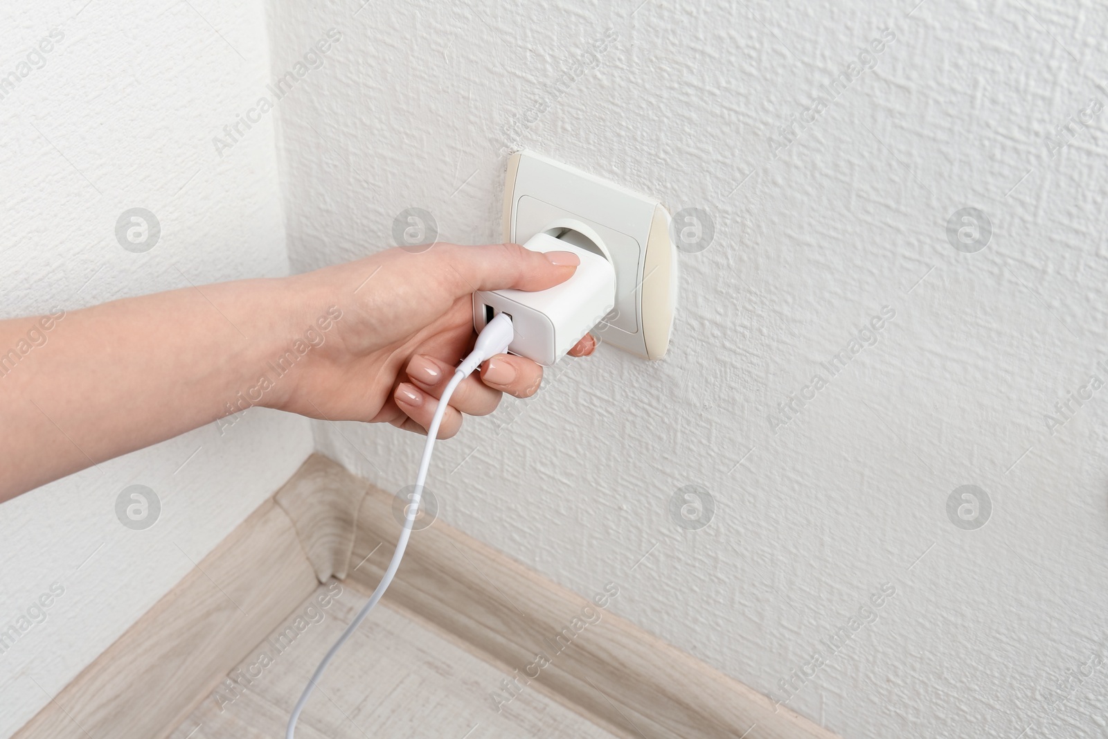 Photo of Woman plugging USB power adapter with charge cable into electrical socket indoors, closeup