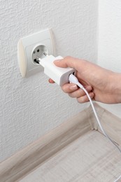 Photo of Woman plugging USB power adapter with charge cable into electrical socket indoors, closeup