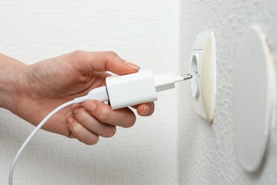 Photo of Woman plugging USB power adapter with charge cable into electrical socket indoors, closeup