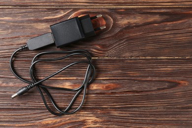 Photo of USB power adapter with charge cable on wooden table, top view. Space for text