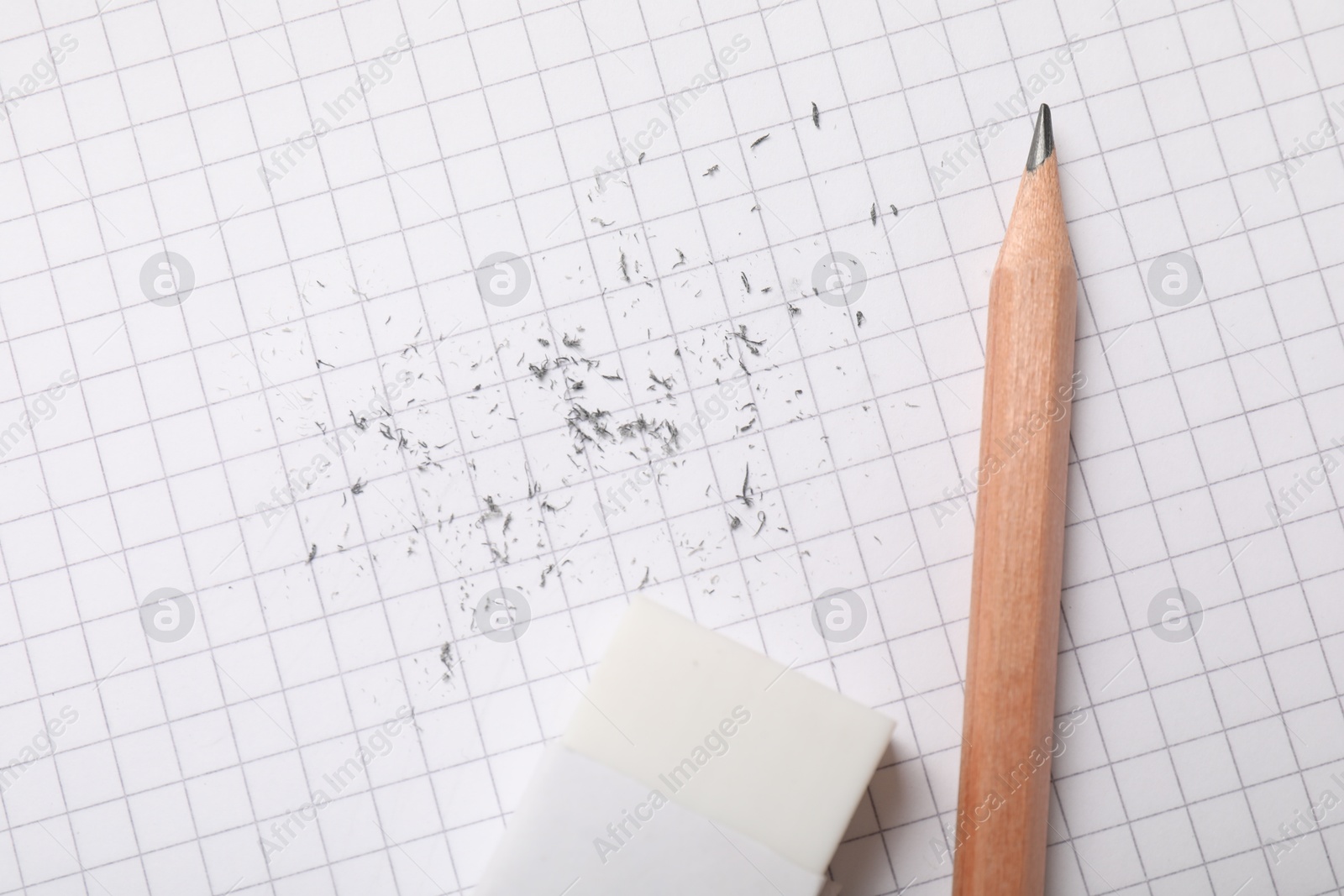 Photo of Eraser, pencil and scraps on checkered notebook sheet, flat lay