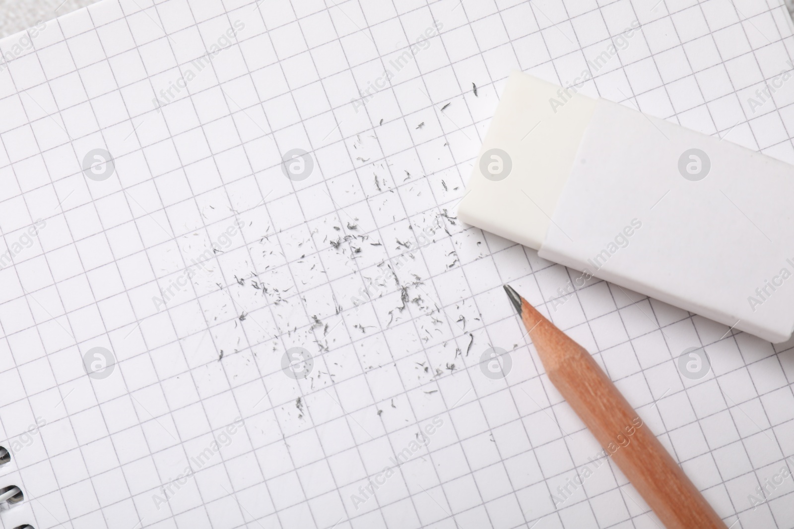 Photo of Eraser, pencil and scraps on checkered notebook sheet, flat lay