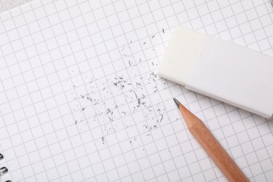 Photo of Eraser, pencil and scraps on checkered notebook sheet, flat lay