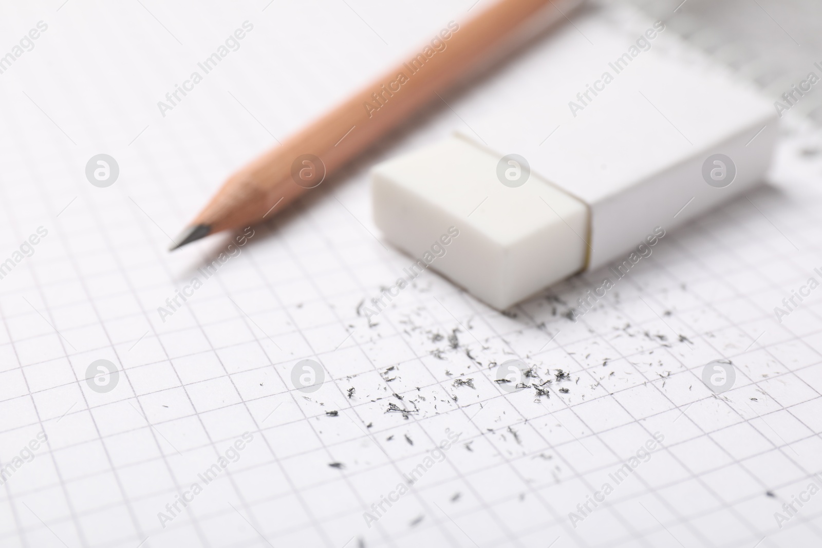 Photo of Eraser, pencil and scraps on checkered notebook sheet, closeup