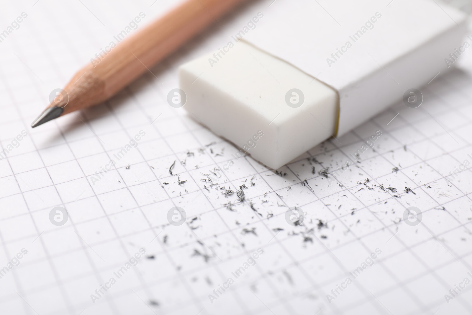 Photo of Eraser, pencil and scraps on checkered notebook sheet, closeup