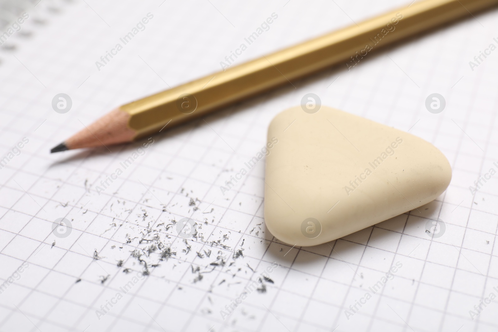 Photo of Eraser, pencil and scraps on checkered notebook sheet, closeup