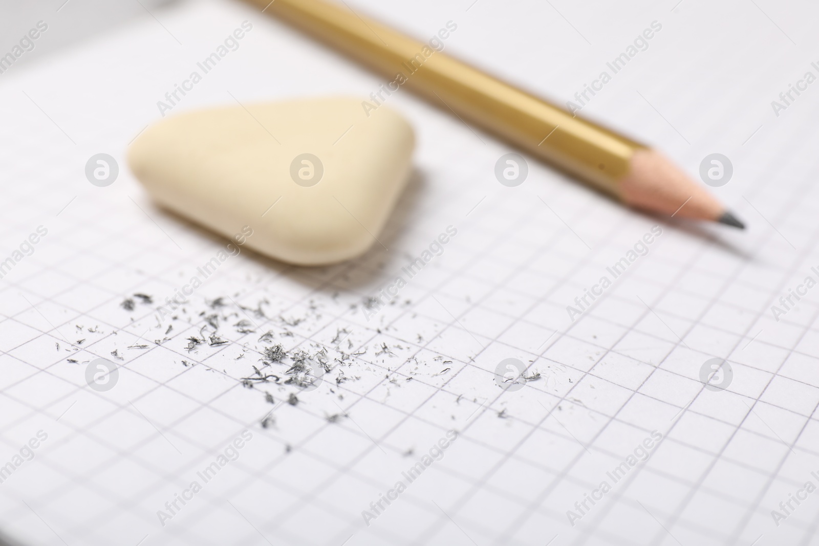 Photo of Eraser, pencil and scraps on checkered notebook sheet, closeup