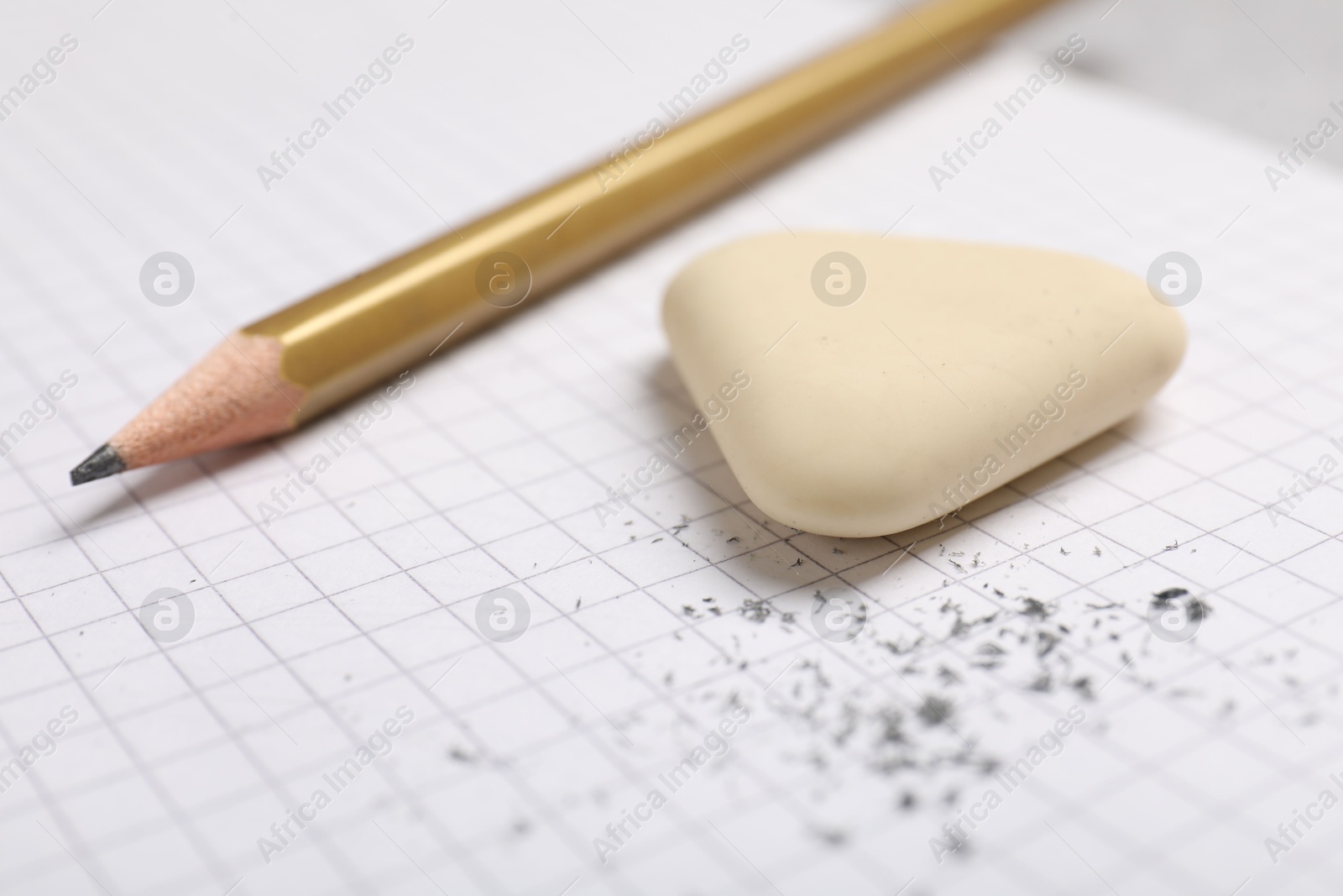 Photo of Eraser, pencil and scraps on checkered notebook sheet, closeup