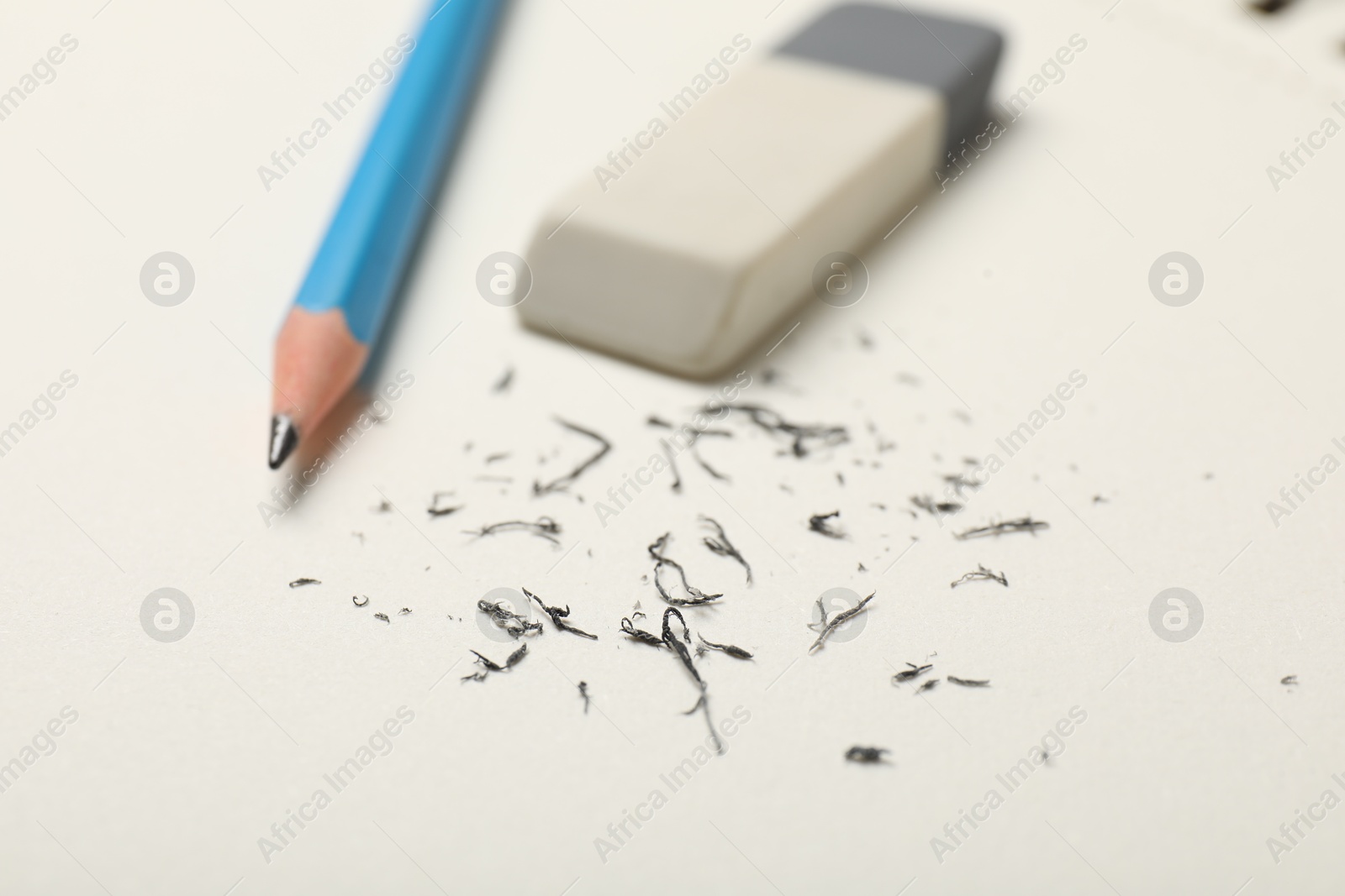 Photo of Eraser, pencil and scraps on white sheet of paper, closeup