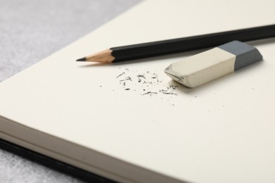 Photo of Eraser, pencil, scraps and notebook on grey table, closeup