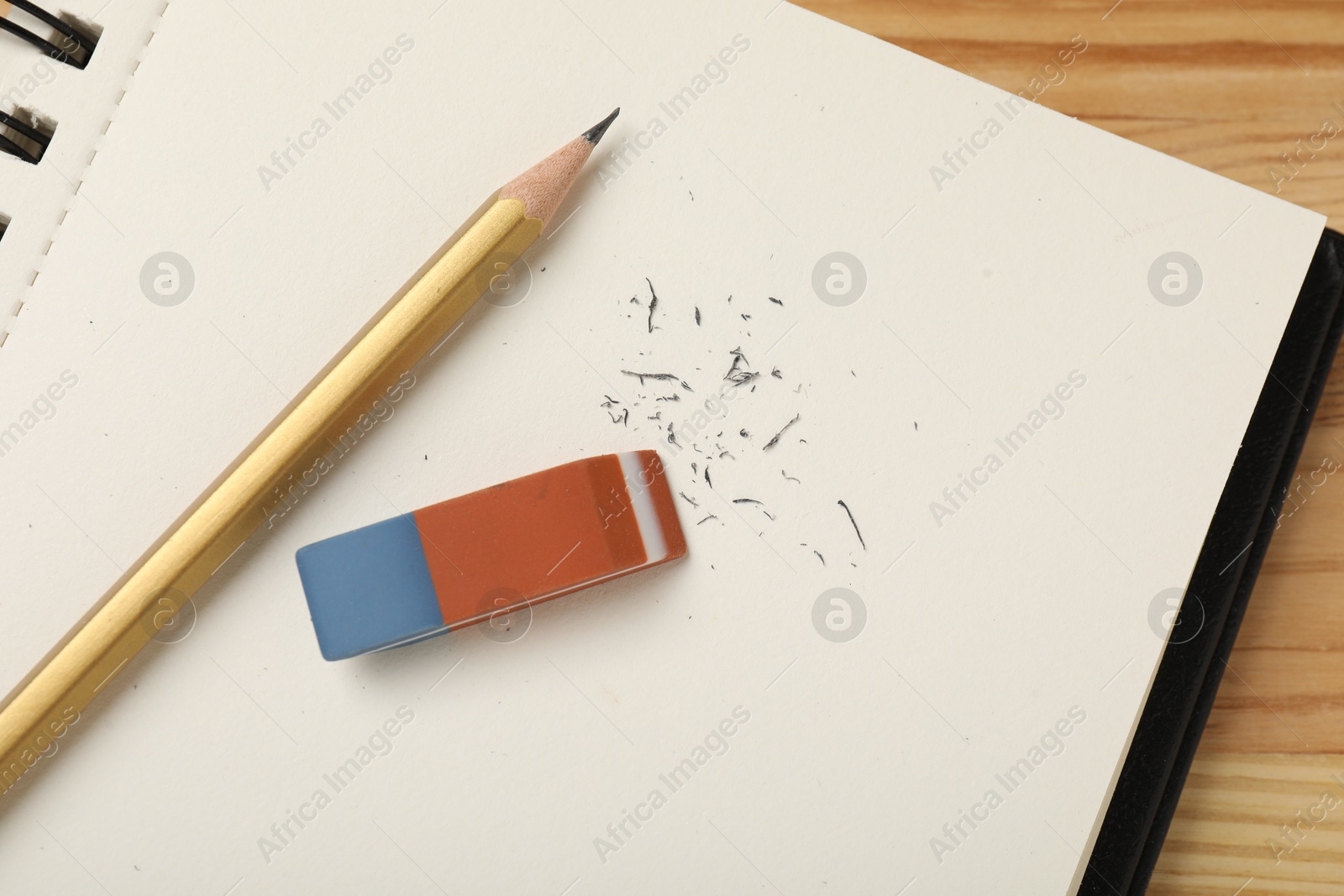 Photo of Eraser, pencil, scraps and notebook on wooden table, top view