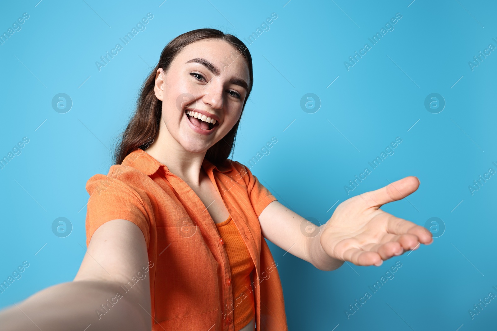 Photo of Happy woman welcoming friends or guests on light blue background, view through front camera of gadget