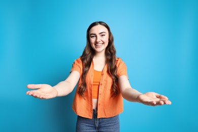 Photo of Happy woman welcoming friends or guests on light blue background