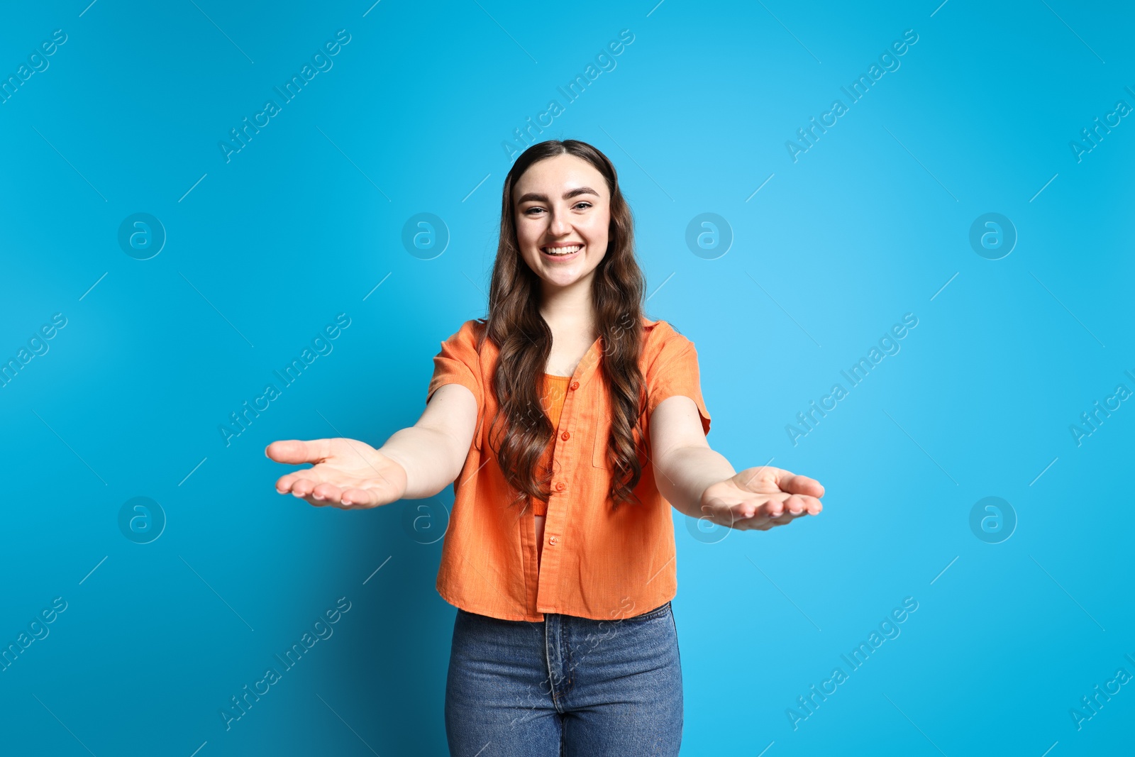 Photo of Happy woman welcoming friends or guests on light blue background