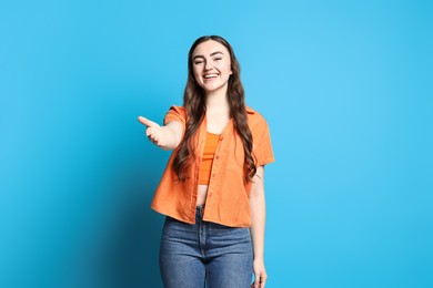 Happy woman welcoming friends or guests on light blue background