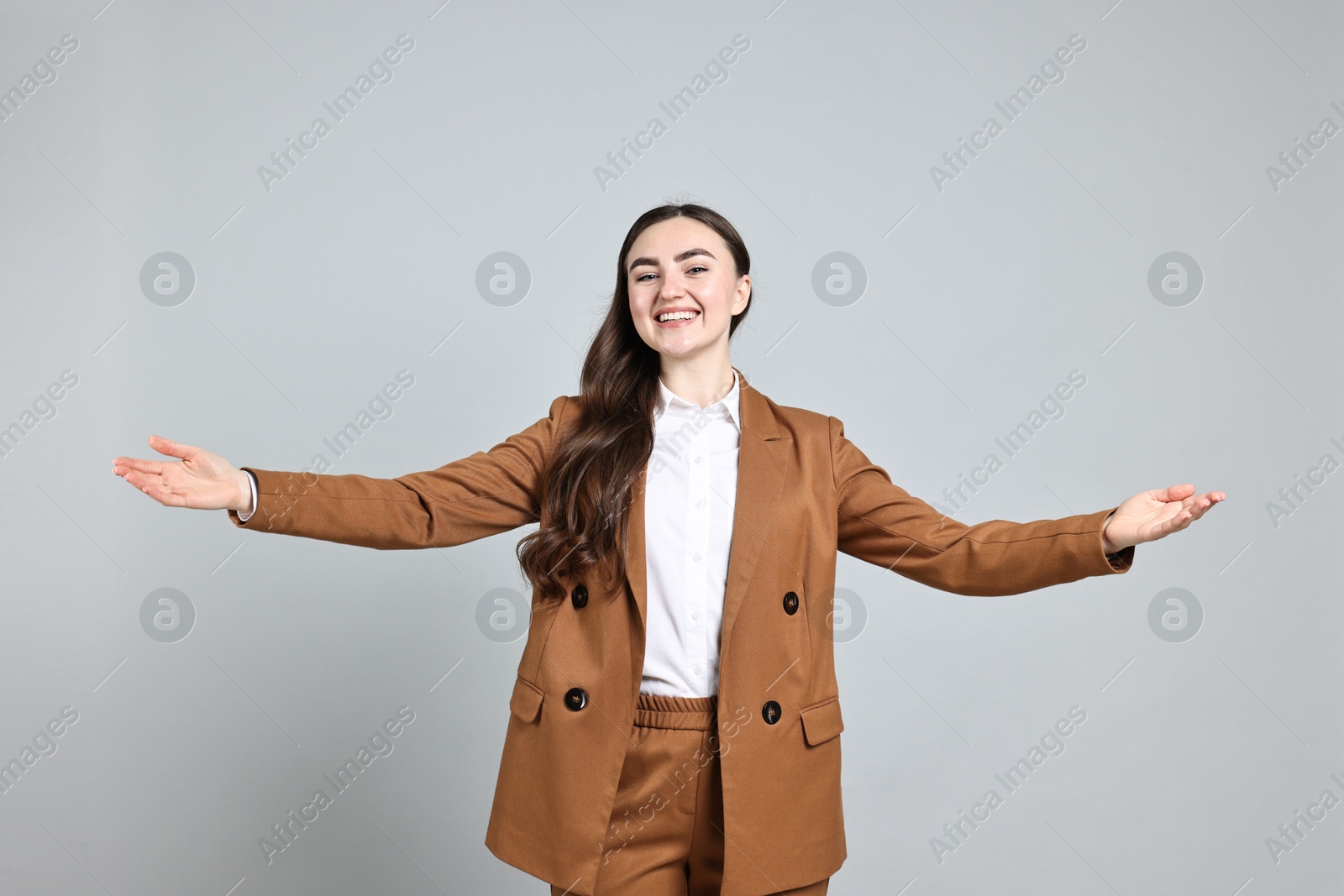 Photo of Happy businesswoman welcoming clients or partners with wide open arms on grey background