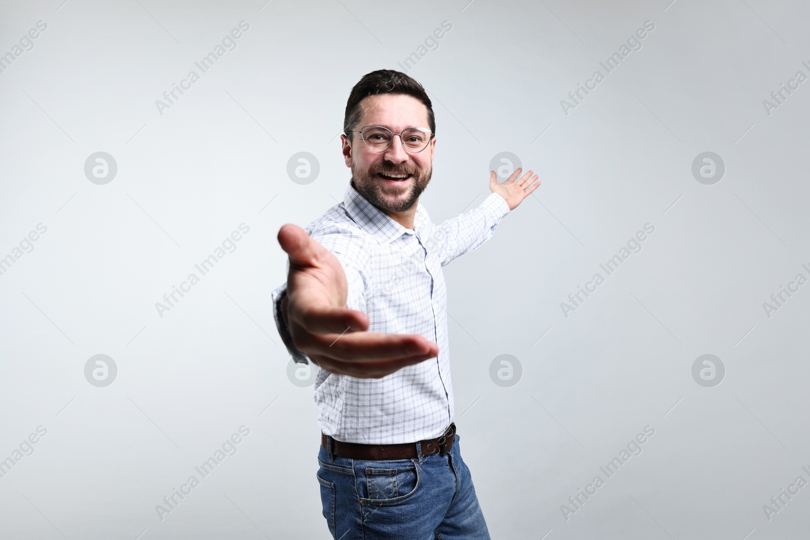 Photo of Happy man welcoming friends or guests on grey background