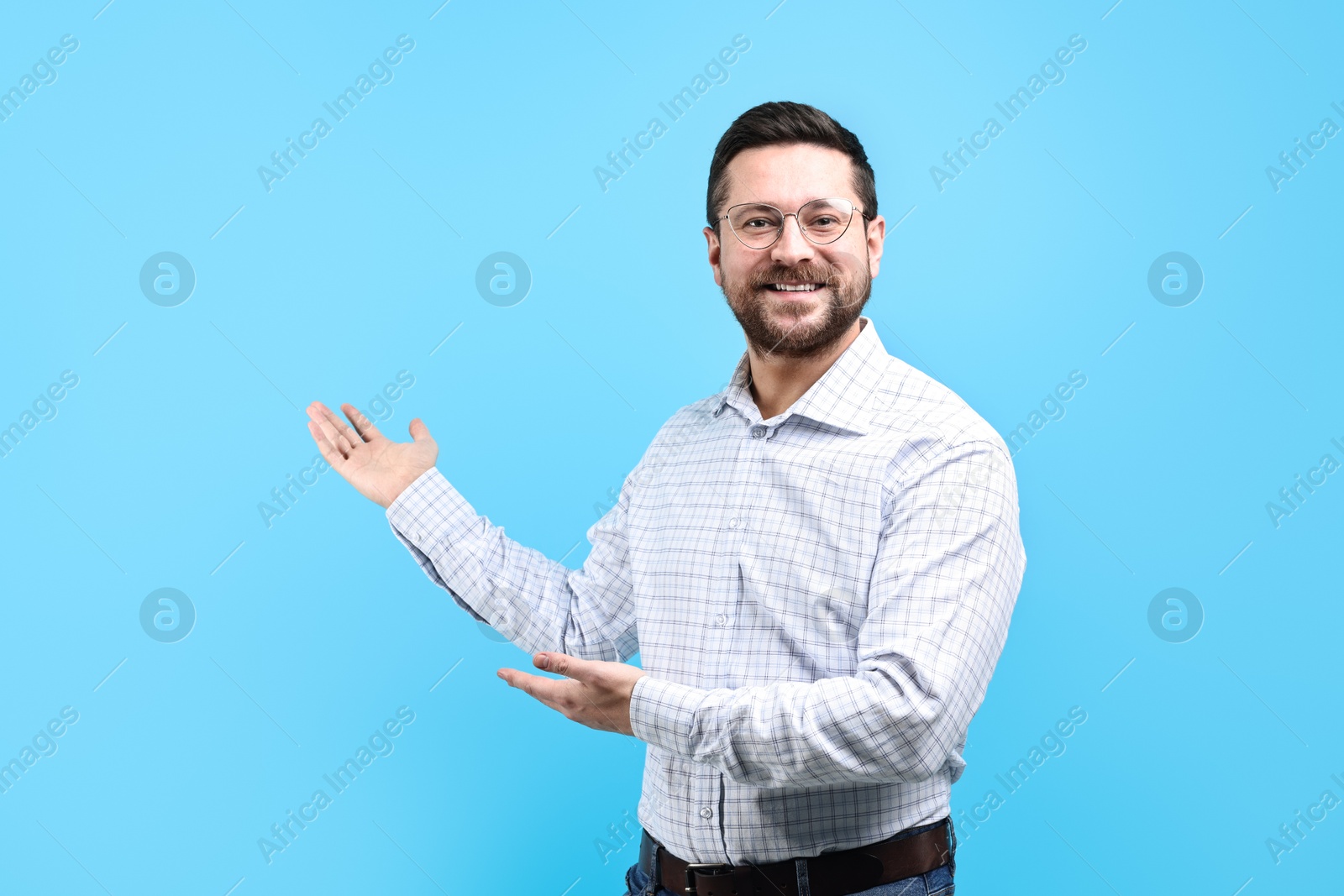 Photo of Happy man welcoming friends or guests on light blue background