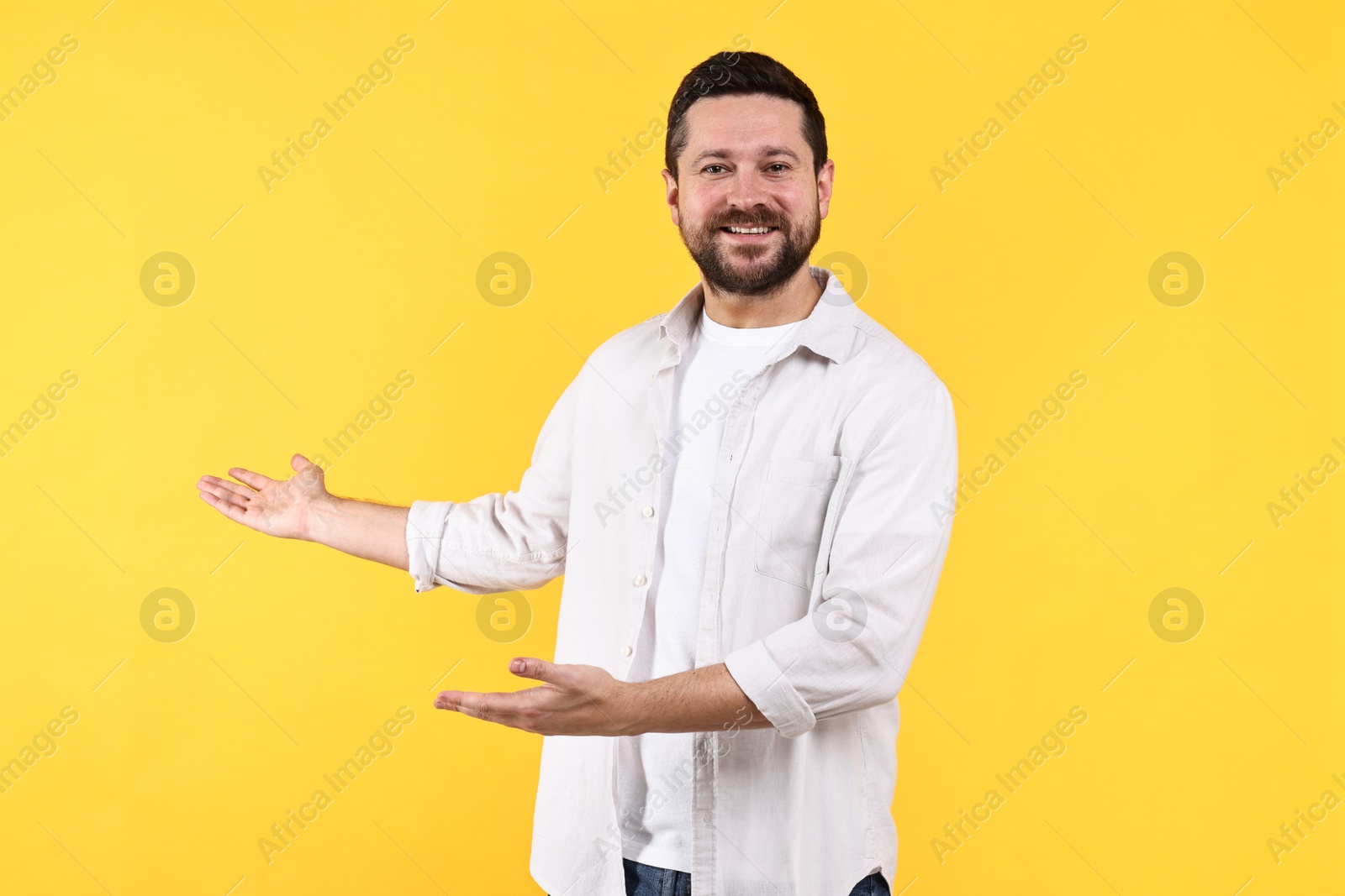 Photo of Happy man welcoming friends or guests on yellow background