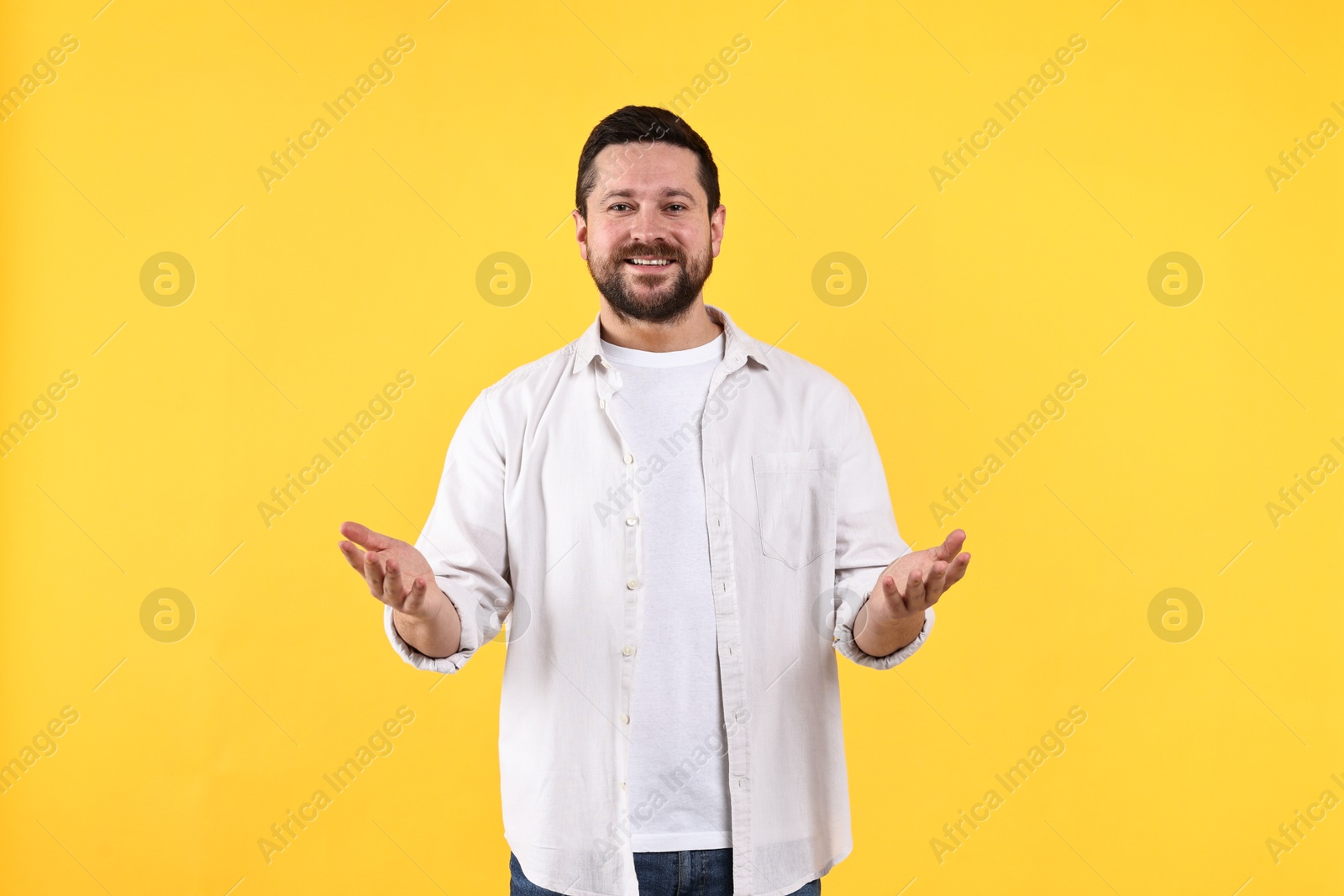 Photo of Happy man welcoming friends or guests on yellow background