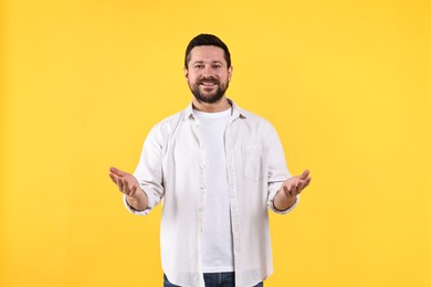 Photo of Happy man welcoming friends or guests on yellow background