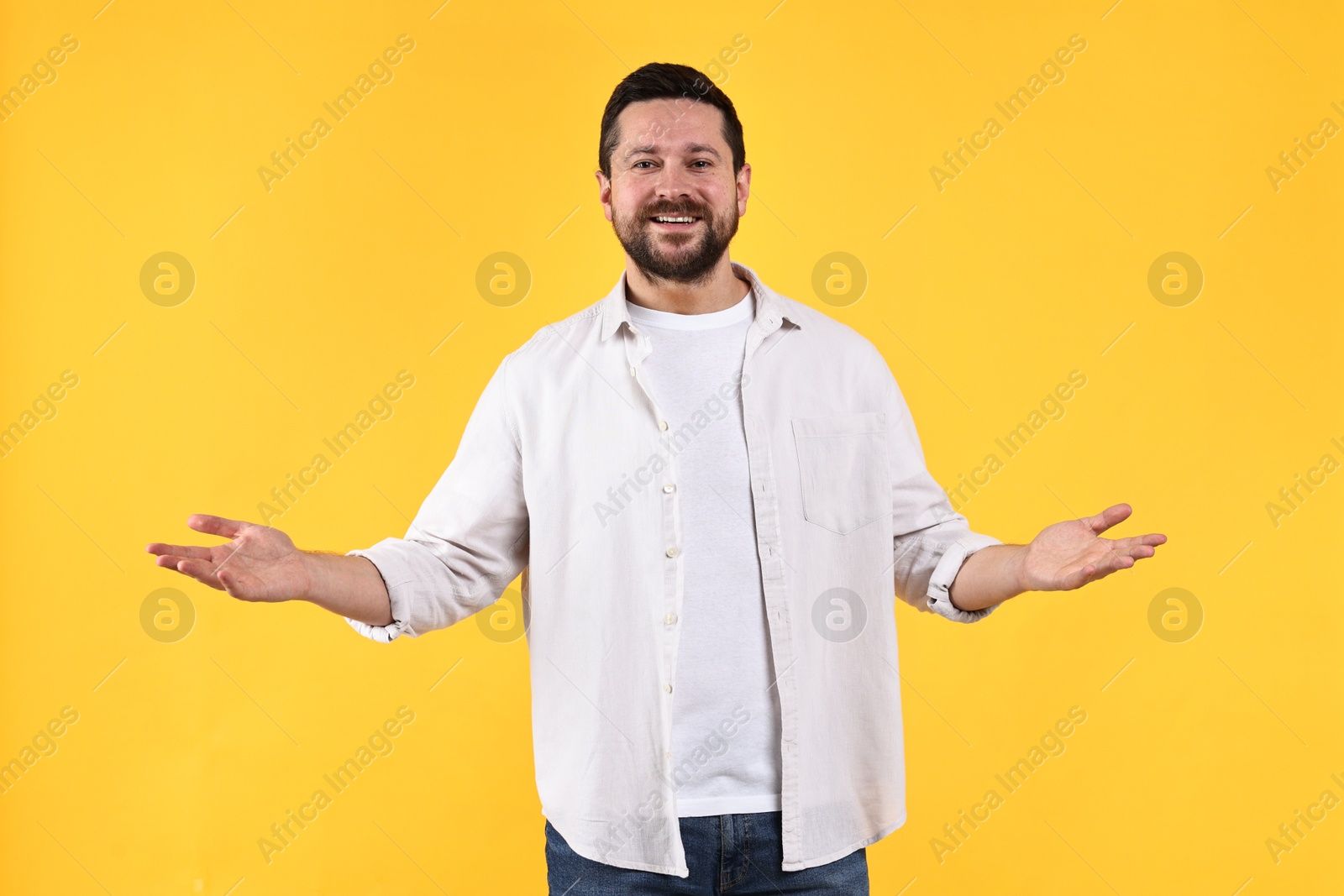 Photo of Happy man welcoming friends or guests on yellow background