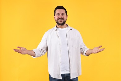 Photo of Happy man welcoming friends or guests on yellow background