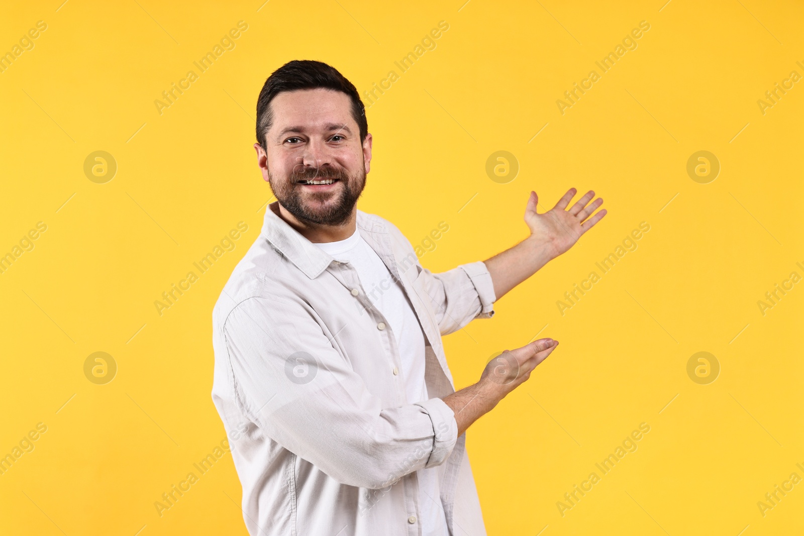 Photo of Happy man welcoming friends or guests on yellow background