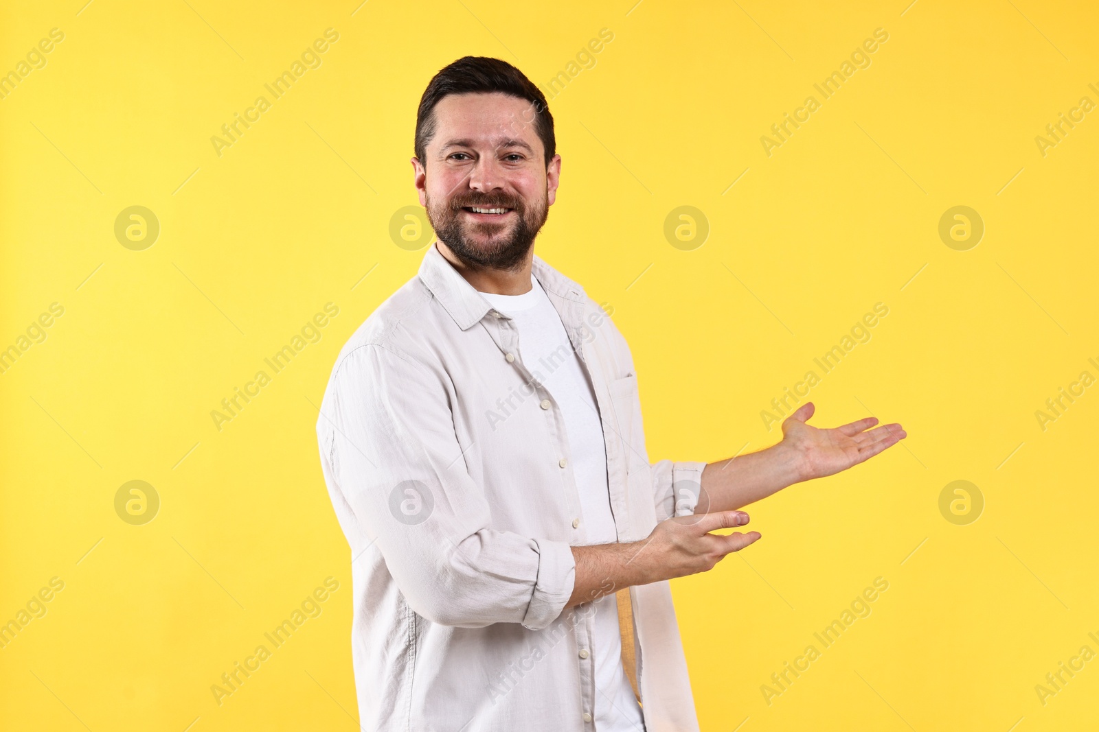 Photo of Happy man welcoming friends or guests on yellow background