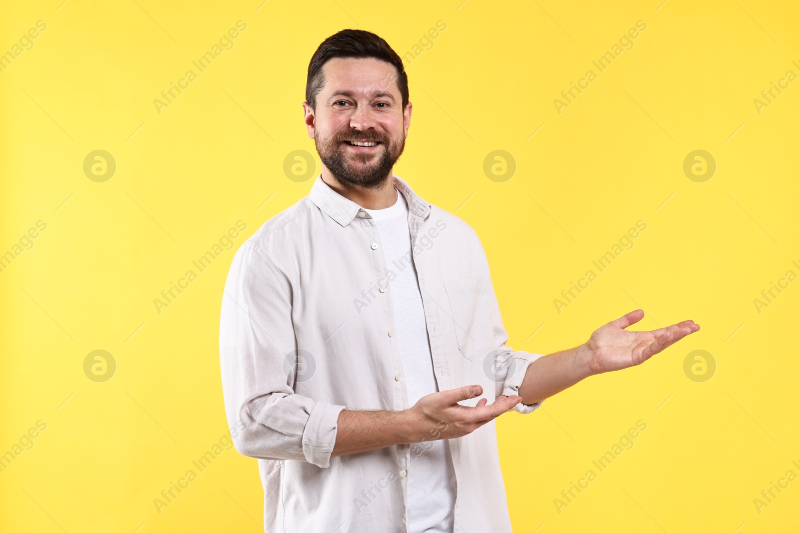 Photo of Happy man welcoming friends or guests on yellow background