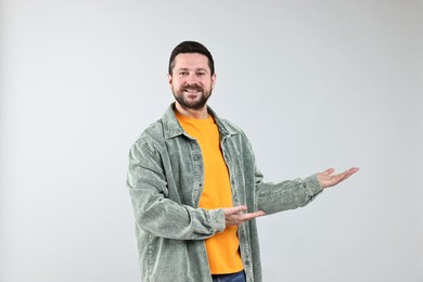 Photo of Happy man welcoming friends or guests on grey background