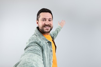 Photo of Happy man taking selfie and welcoming friends or guests on grey background