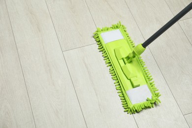 Microfiber mop on wooden floor, space for text